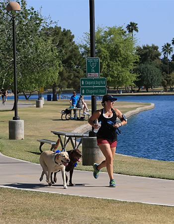 women running with dog on leash past a lake on a shared use path