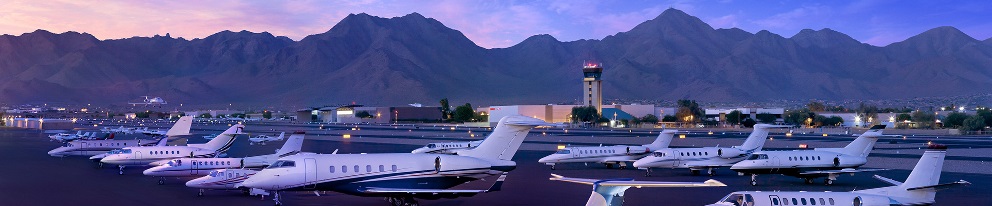 Private jets parked at Scottsdale Airport with mountains and a control tower in the background.