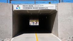 People walk through the Chaparral Road Underpass on the Indian Bend Wash Path, a concrete tunnel with a paved trail leading to daylight at the far end.