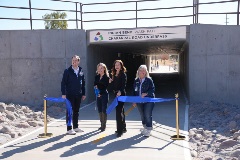 Four people hold a blue ribbon at the entrance of the Chaparral Road Underpass on the Indian Bend Wash Path during a ribbon-cutting ceremony.