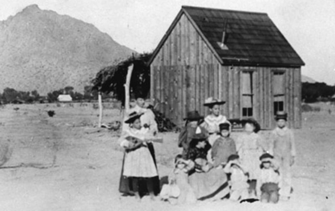 School children and teachers posing for a portrait in front of the old school house.