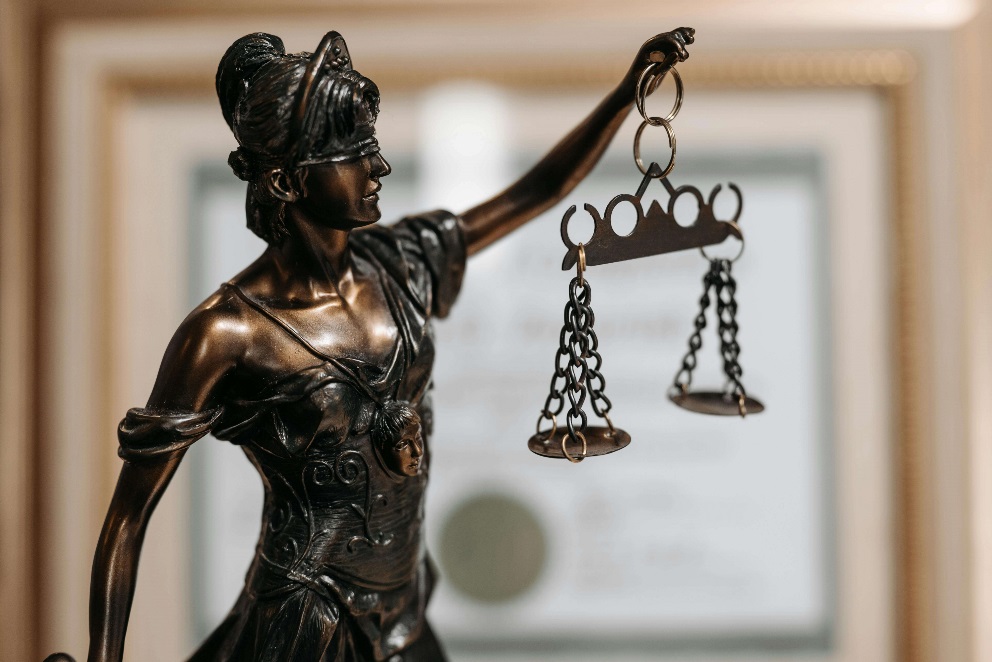 A close-up photo of a bronze statue of Lady Justice, featuring a blindfolded figure holding balanced scales, symbolizing the fair and equal administration of the law without corruption, avarice, prejudice, or favor.