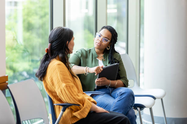 Two women talking in a bright office waiting area, one holding a tablet.