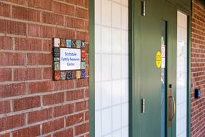 Entrance to Scottsdale Family Resource Center with brick wall, green door, and small sign.