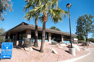 Single-story building with large windows, palm trees, and nearby directional sign on desert landscaping.
