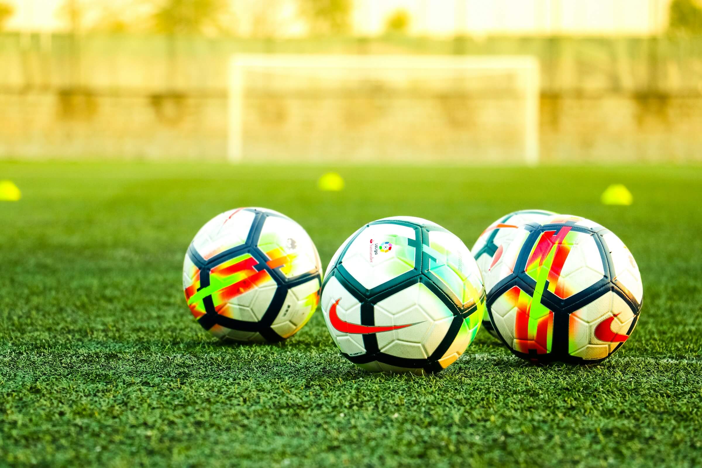 Three colorful soccer balls on a grass field with a blurred goal in the background.