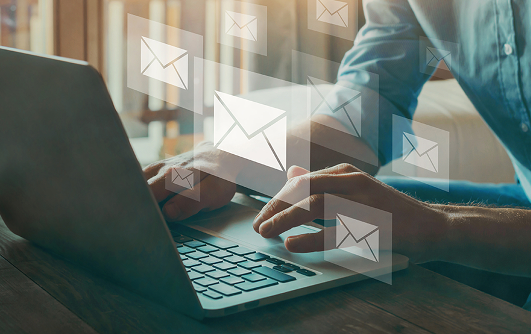 Hands typing on laptop with email icons floating around