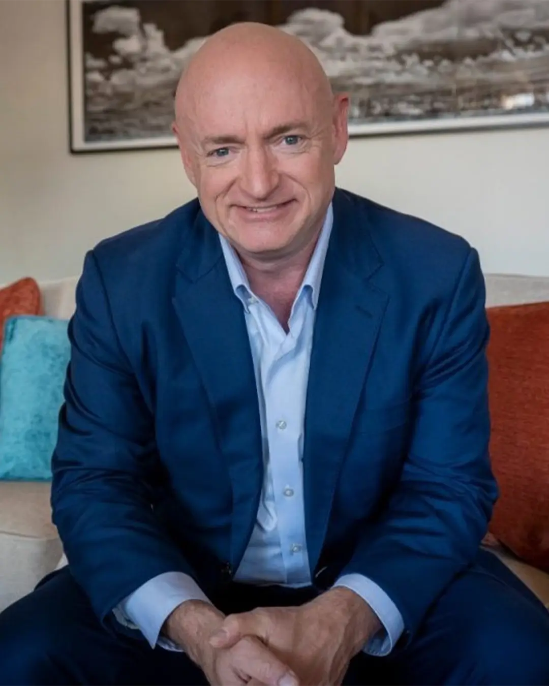 A portrait of Senator Mark Kelly seated on a sofa and smiling.