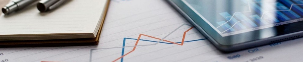 Notebook and pens beside a tablet displaying an upward-trending line chart on a financial report background.