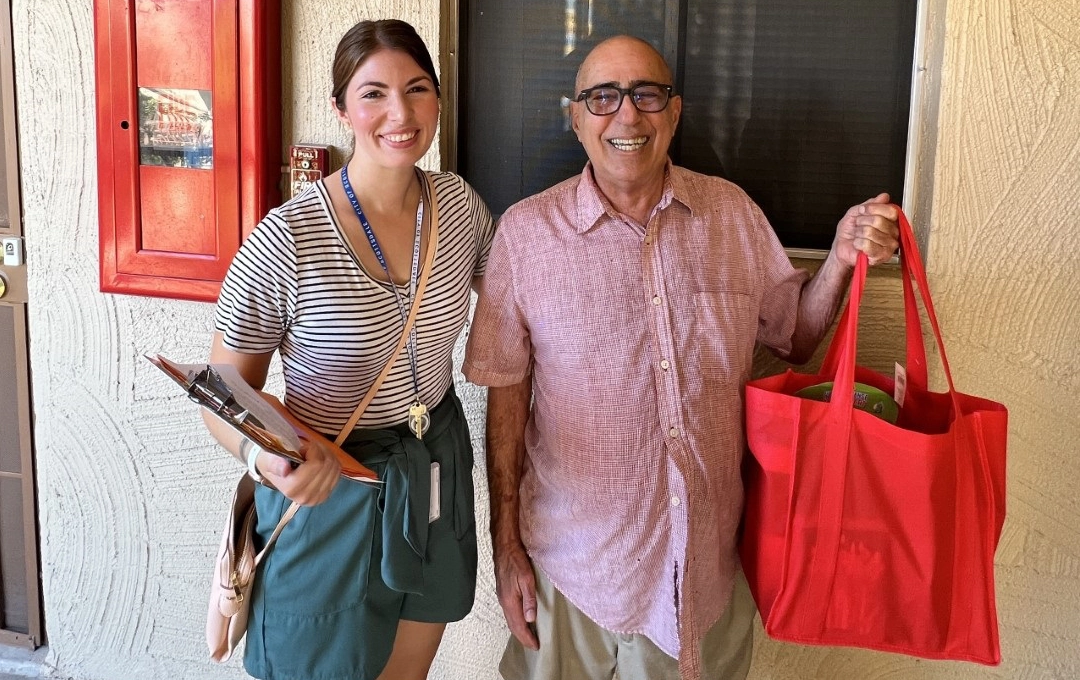 News image Female staff and Scottsdale senior in front of apartment holding red bag of supplies
