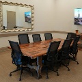 A conference room with a rustic wood table, eight black mesh chairs, a wall-mounted TV and a large silver-framed mirror.