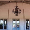 A wrought iron chandelier hangs from a beamed patio ceiling in front of a wall of glass doors.