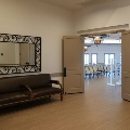 A lobby with a leather bench under a wrought iron mirror and open double doors leading to a ballroom set with rows of chairs.