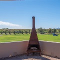 A rusted metal chimenea sits in the corner of a patio overlooking a large green field, parked RVs and desert hills.