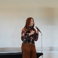 A speaker in a floral top talks into a microphone next to a speaker on a stand.