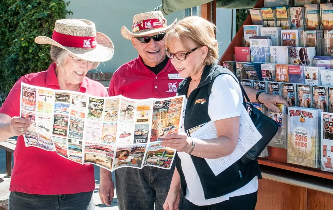 News image Three volunteers in hats help a visitor read a city map beside brochure stand.