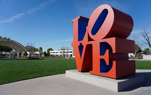 Large red LOVE sculpture in a sunny outdoor park with clear blue skies