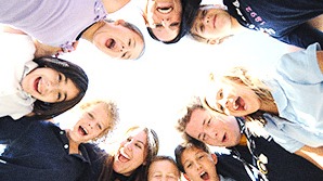 Smiling children standing in a circle, looking down toward the camera against bright sky.
