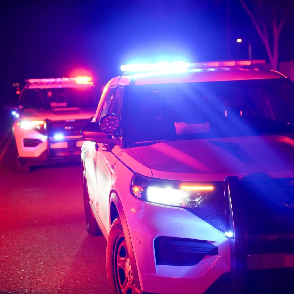 Twopolicecruisersparkedonaroadatnightwiththeirredandblueemergencylightsflashing