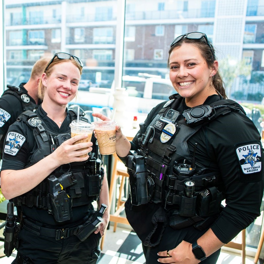 TwosmilingScottsdalepoliceofficersinuniformholdupicedcoffeedrinksindoors