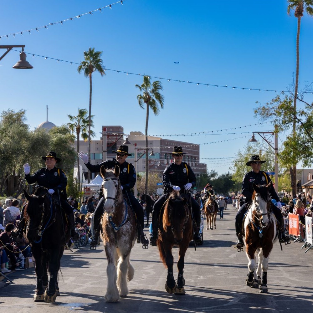 FourScottsdalemountedpoliceofficersridehorsesdownasunnycitystreetduringaparade