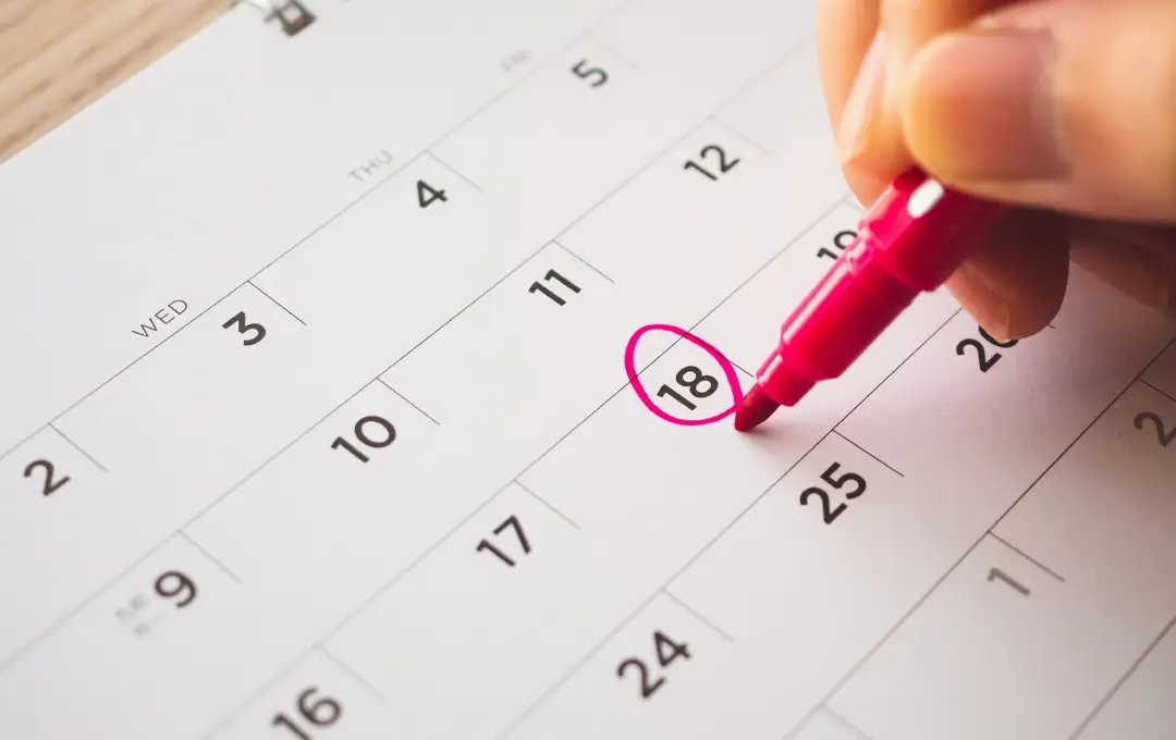 Hand using pink marker to circle the 18th on a monthly calendar page.