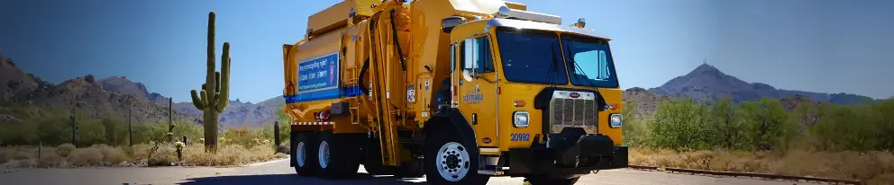 A yellow Scottsdale solid waste truck on a desert road with a "Are you recycling right?" message. Saguaro cacti and mountainous terrain under a clear blue sky in the background.