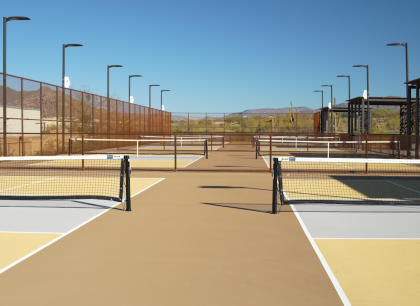 Outdoor pickleball courts with nets, tall fencing, and surrounding desert landscape under a clear sky.
