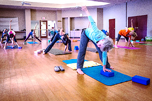 Group of adults in a bright studio practicing yoga poses on mats with blocks.