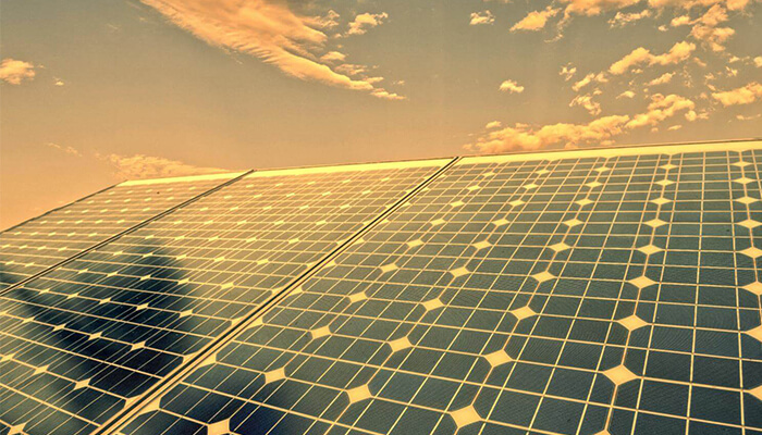 Solar panels reflecting warm sunlight beneath a partly cloudy sky during golden hour.