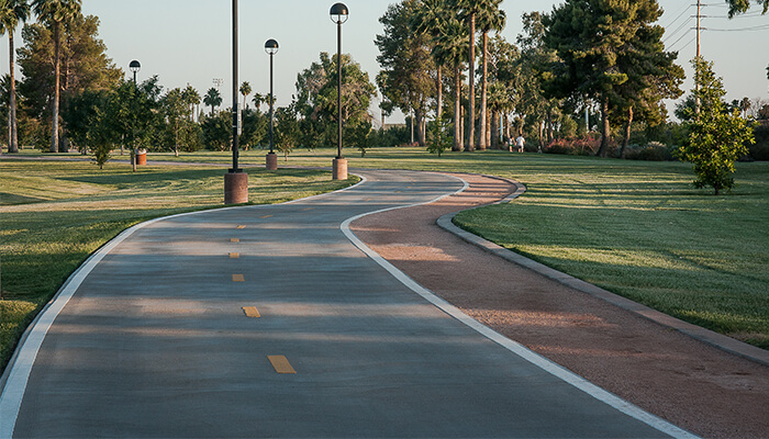 Smooth walking and biking path weaving through open lawns, trees, and shaded park areas.