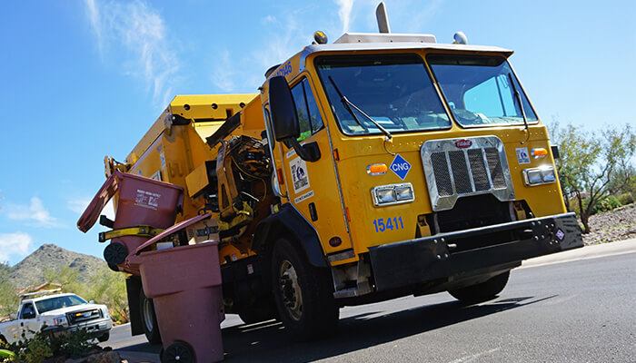 A city waste collection truck lifts residential bins during a routine neighborhood pickup.