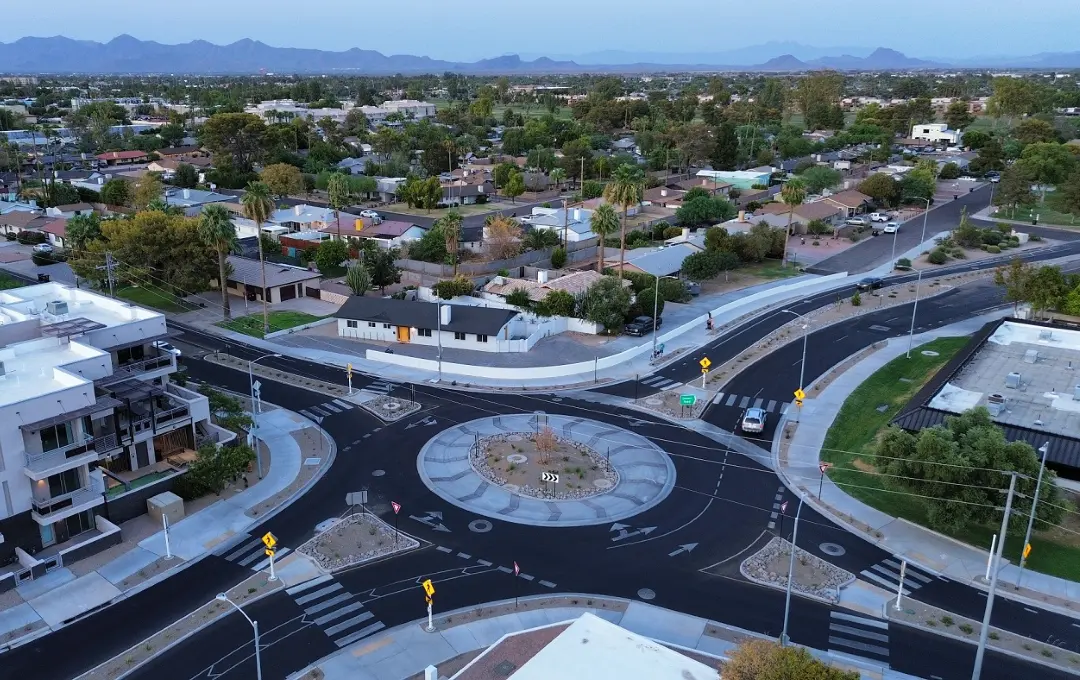 Aerial view of a newly constructed roundabout surrounded by residential neighborhoods, palm trees, and distant mountains.