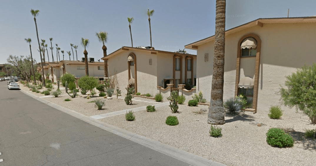 Apartmentbuildingswithsparsedesertlandscapingalongaresidentialstreetfeaturinggravelgroundcoverpalmtreescactiandsmallshrubsunderaclearsky